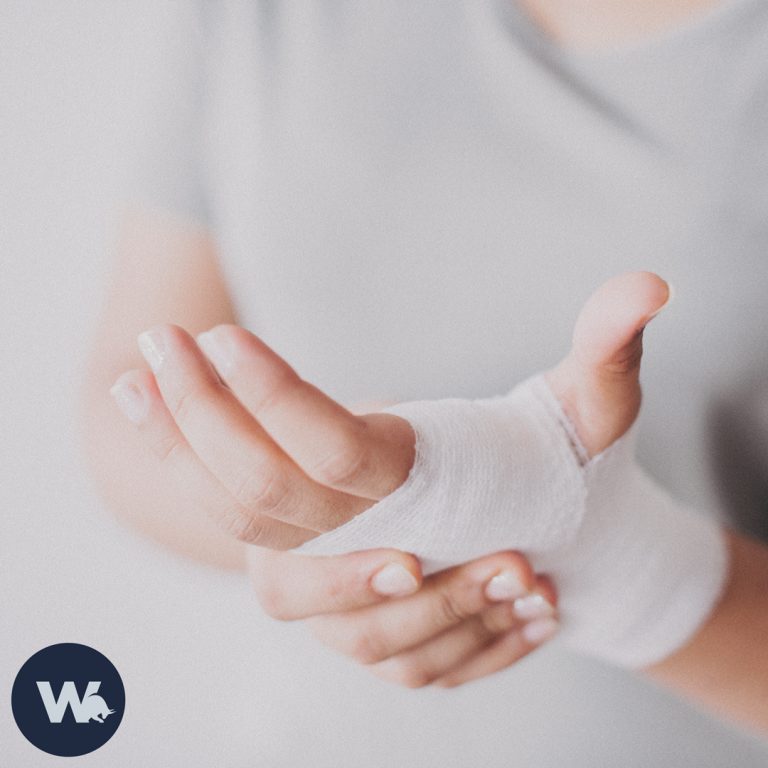 Eine Frau hält mit der Hand ihre andere bandagierte Hand. Die verletzte Stelle scheint zu schmerzen.
